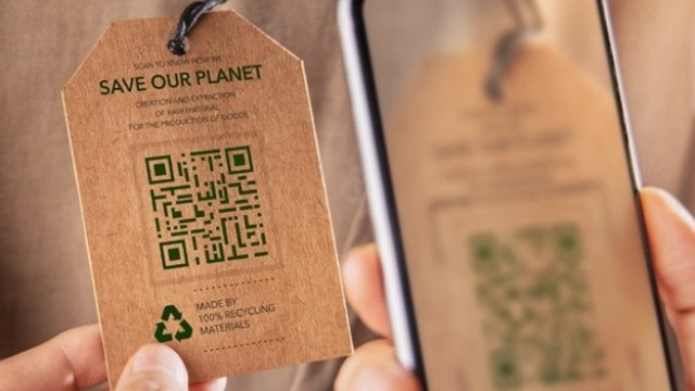 Osoba skanuje smartfonem kod QR z metki ubrania z napisem 'Save our planet' zawierającej informacje o zrównoważonej produkcji