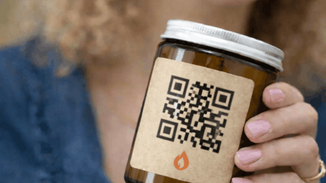 Kobieta trzymająca w dłoni szklany słoik z etykietą, na której znajduje się duży kod QR służący do uzyskania dodatkowych informacji o produkcie.
