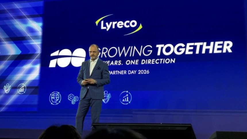Mężczyzna w garniturze przemawia na scenie podczas konferencji. W tle duży, niebieski ekran z logo Lyreco i hasłem "100 Growing Together, Years. One Direction, Partner Day 2026".