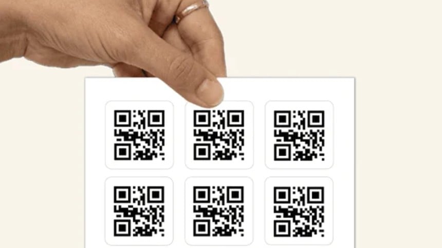 Dłoń trzyma arkusz z kwadratowymi etykietami z nadrukowanymi kodami QR.