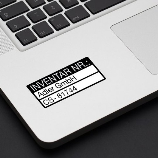 Tabliczka inwentaryzacyjna z informacjami o sprzęcie naklejona na srebrnego laptopa