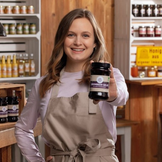 Kobieta prezentująca słoik przetworów z wieloma produktami spożywczymi na półkach w tle