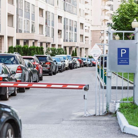 Grafika przedstawia zamknięte osiedle oraz wjazd na którym jest niebieskie oznakowanie parkingu