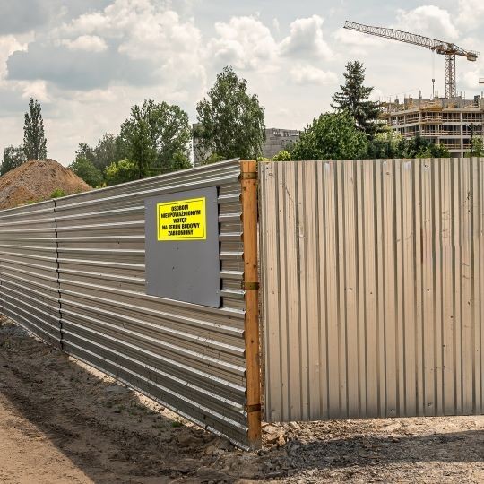 Metalowy płot odgradzający plac budowy z żółtą naklejką ostrzegawczą
