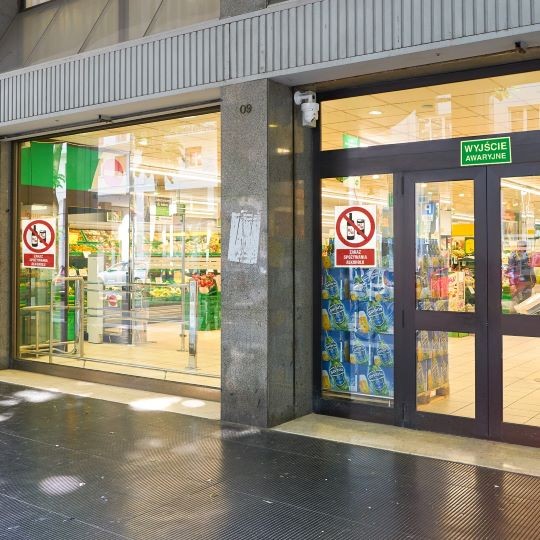 Szklana ściana i drzwi sklepu na których naklejone są znaki zakazu palenia i spożywania alkoholu
