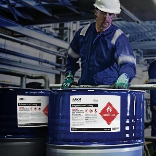 Dwie metalowe beczki z niebiezpiecznymi materiałami zawierające piktogramy chemiczne / Znaki GHS i ADR przy której stoi mężczyzna w ubraniach zabezpieczających