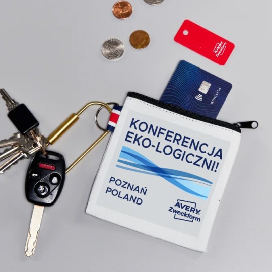 Biała portmonetka z naklejką z nadrukiem kilku skrzyżowanych niebieskim linii o różnym natężeniu koloru, logiem Avery Zweckform i podpisem Konferencja Eko-logiczni Poznan Poland z której wystaje karta płatnicza oraz obok leżące kluczyki od samochodu
