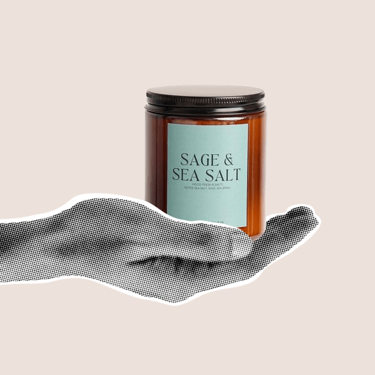 Czarnobiała dłoń trzymająca słoik ze świecą z napisem sage sea and salt