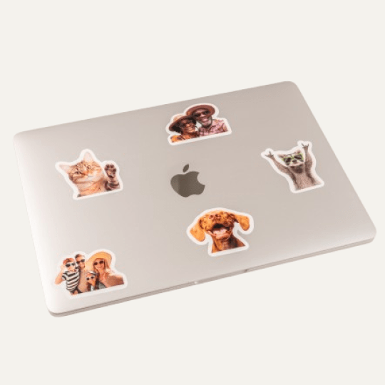 Srebrny laptop z logiem Apple oraz naklejonymi pięcioma naklejkami z kotkiem, pieskami, szopem i dziećmi