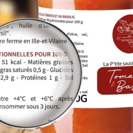  Zbliżenie etykiety sosu pomidorowego z bazylią na słoiku, tekst „Tomate & Basilic”. Przed słoikiem lupa powiększająca fragment informacji o wartościach odżywczych.
