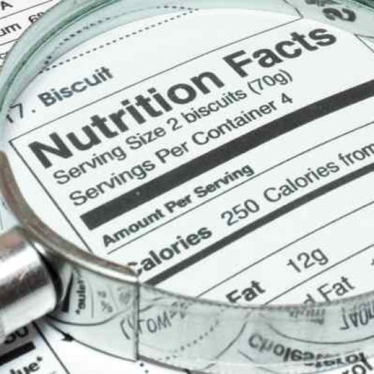 Powiększenie lupą fragmentu tabeli wartości odżywczych na opakowaniu produktu spożywczego, widoczny nagłówek „Nutrition Facts” i niektóre liczby kalorii.