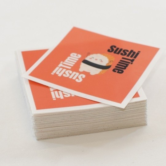 Stos kwadratowych naklejek na białym tle. Na wierzchu naklejka z pomarańczowym tłem, ilustracją uśmiechniętego sushi i czarnym napisem 'Sushi time'.