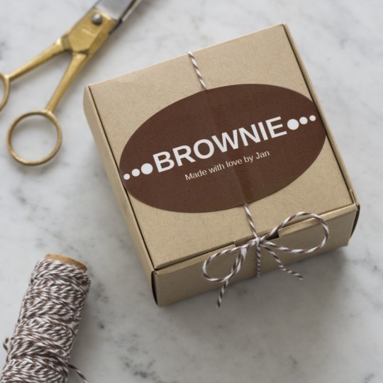Małe, kartonowe pudełko owinięte sznurkiem, z brązową etykietą z napisem „Brownie – Made with love by Jan”. W tle nożyczki i sznurek na marmurowym blacie.