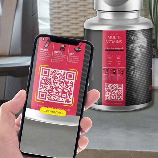 Dłoń trzymająca smartfon z włączonym aparatem skanującym duży czerwony kod QR na etykiecie suplementu diety, w tle widoczna butelka z tą samą etykietą, co pokazuje użycie kodu do uzyskania informacji o multiwitaminach