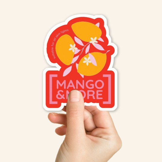 Dłoń trzymająca pojedynczą naklejkę o niestandardowym kształcie (die-cut). Na naklejce znajduje się grafika z mango i napis "MANGO & MORE".