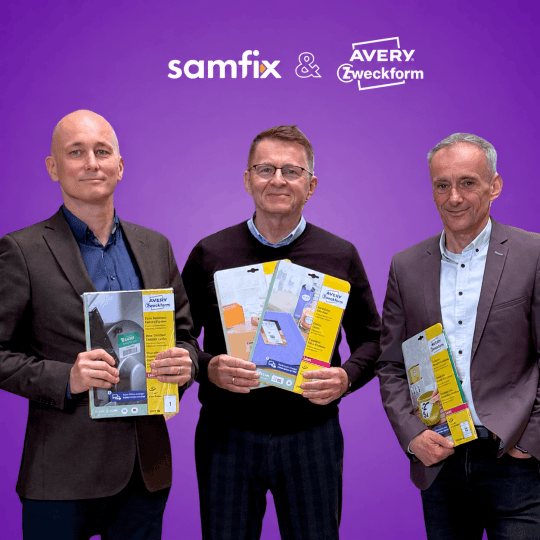 Grafika promocyjna na fioletowym tle z napisem "Samfix & AVERY Zweckform". Poniżej stoją trzej mężczyźni, przedstawiciele firm, uśmiechają się i trzymają w rękach produkty – etykiety Avery Zweckform.