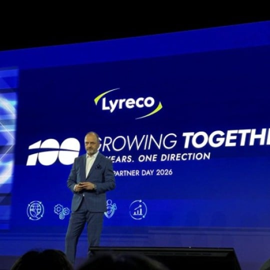 Mężczyzna w garniturze przemawia na scenie podczas konferencji. W tle duży, niebieski ekran z logo Lyreco i hasłem "100 Growing Together, Years. One Direction, Partner Day 2026".