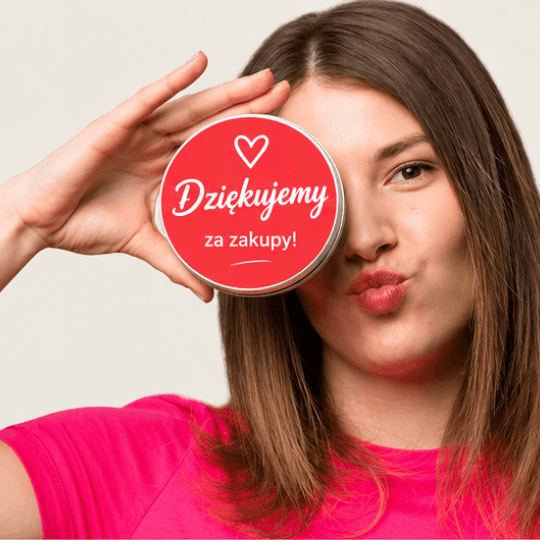 Kobieta trzymająca przy oku okrągłą czerwoną naklejkę z symbolem serca i napisem „Dziękujemy za zakupy!