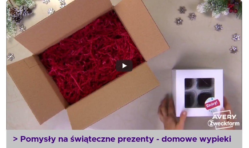 Otwarty karton z czerwonymi ścinkami papieru oraz dłonie trzymające białą paczkę pralinek