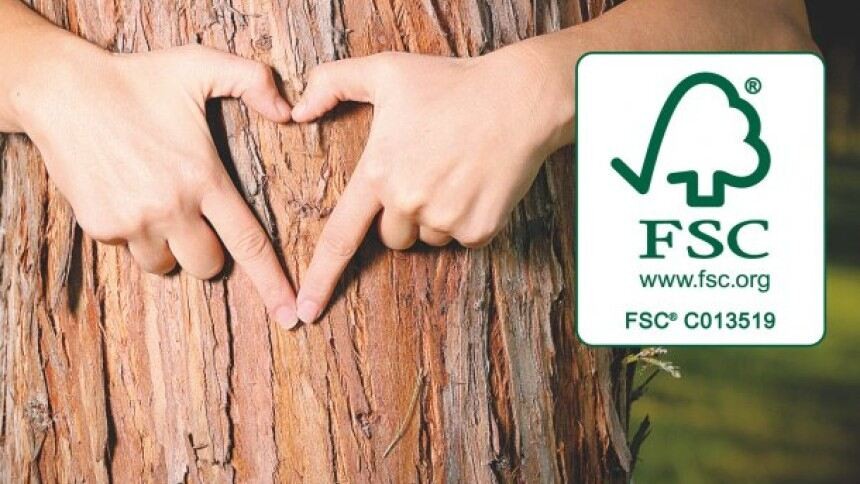 Dwie dłonie układające się w kształt serca z drewnianą powierzchnią w tle wraz z symbolem FSC po prawej