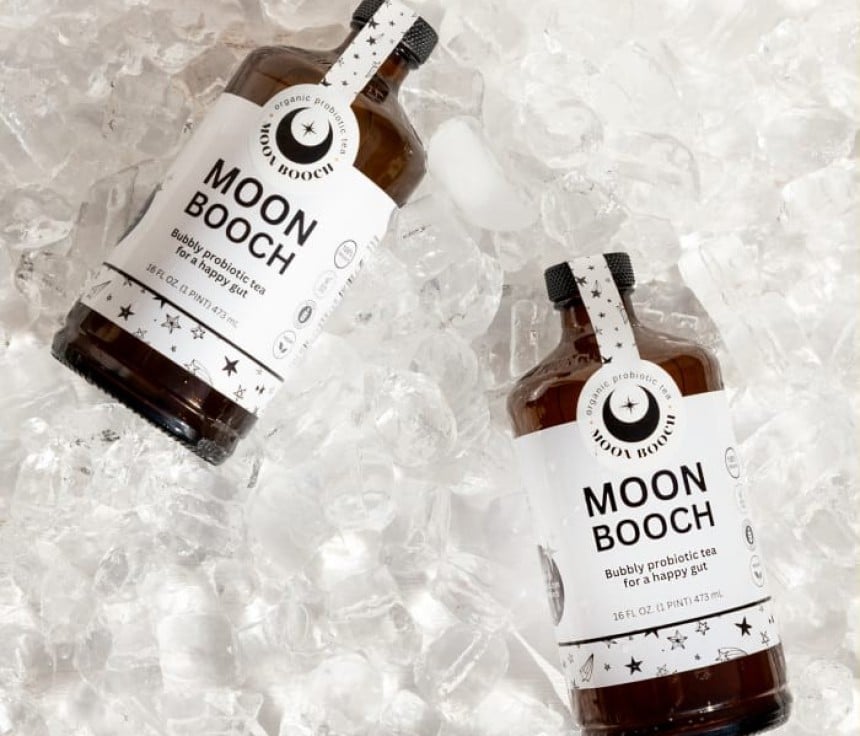 Dwie brązowe butelki z napisem Moon Booch na białej etykiecie położone na kostkach lodu