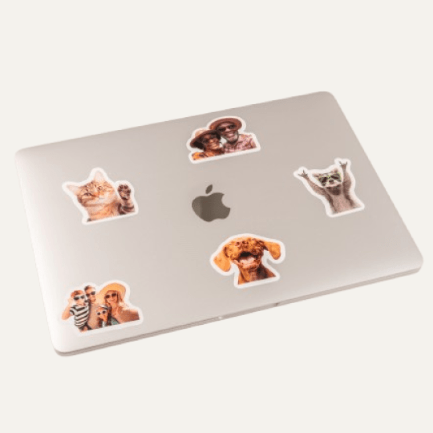 Srebrny laptop z logiem Apple oraz naklejonymi pięcioma naklejkami z kotkiem, pieskami, szopem i dziećmi