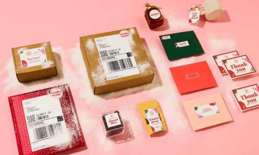 Różne paczki, koperty i kartki z etykietami na różowym tle, posypane sztucznym śniegiem. Wśród nich znajdują się podziękowania, karty prezentowe, paczka miodu i opakowania świąteczne.