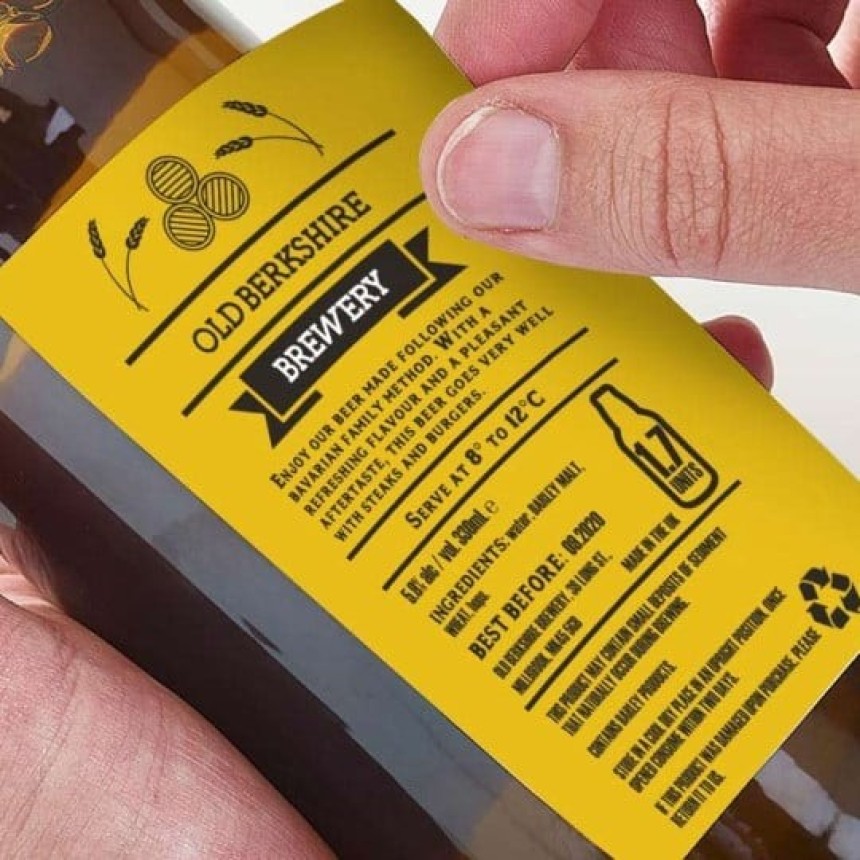 Zbliżenie butelki piwa trzymanej w rękach, żółta etykieta z widocznymi informacjami o produkcie „Old Berkshire Brewery”, zaleceniami serwowania i datą ważności.