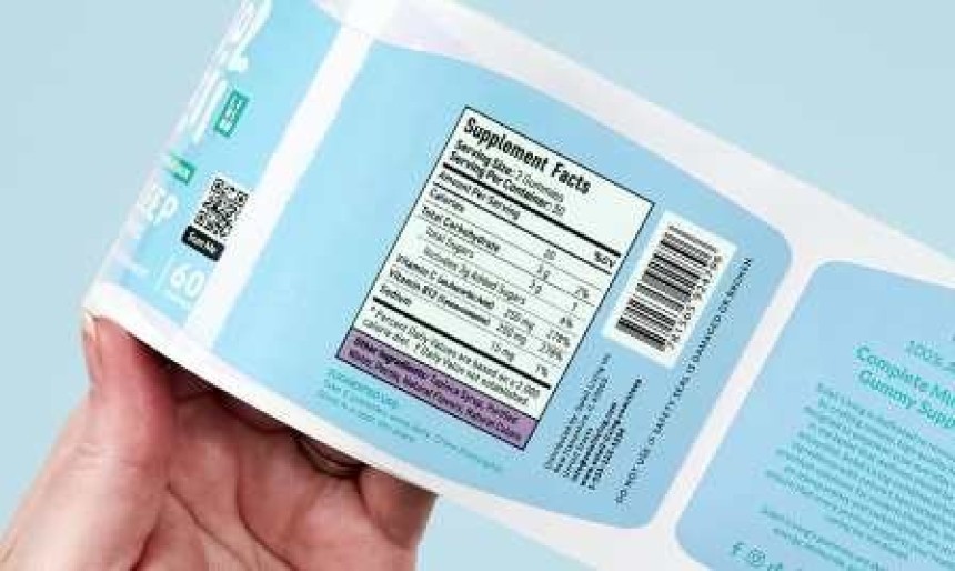 Ręka trzymająca produkt z niebieską etykietą, na której widać tabelę „Supplement Facts” i kod kreskowy.