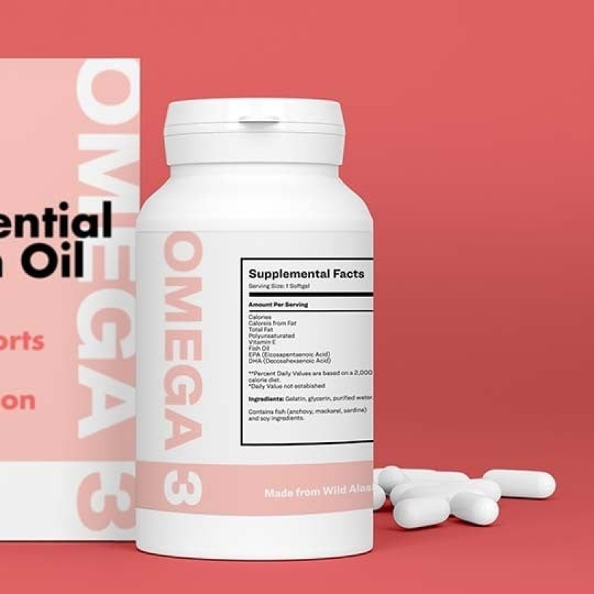 Białe opakowanie suplementu diety Omega 3 na różowym tle, obok opakowania leży kilka białych kapsułek. Na butelce widoczna tabela „Supplemental Facts” z informacjami o wartościach odżywczych oraz napis „Made from Wild Alaskan Fish Oil”.