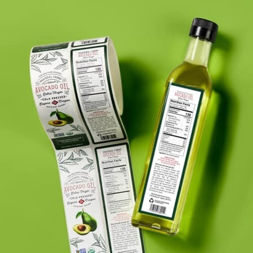 Butelka oleju z awokado obok rolki etykiet; z tyłu etykiety tabela Nutrition Facts — przykład projektu etykiety produktu spożywczego.