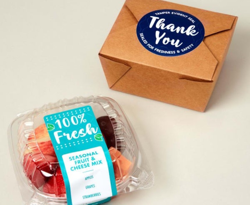 Opakowanie z przezroczystego plastiku z pokrojonymi owocami oraz kartonowe pudełko, oba z dużymi kolorowymi naklejkami; na owocach napis „100% Fresh”, a na pudełku „Thank You”.