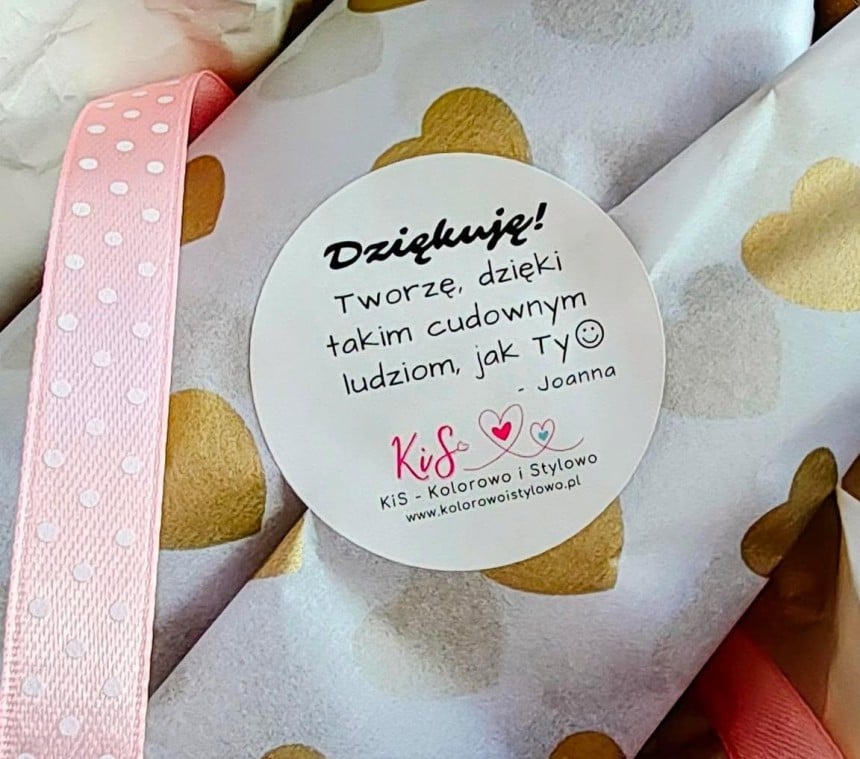 Prezent owinięty w biały papier w złote serduszka. Na nim okrągła naklejka z napisem: "Dziękuję! Tworzę, dzięki takim cudownym ludziom, jak Ty - Joanna" oraz logo "KiS - Kolorowo i Stylowo".