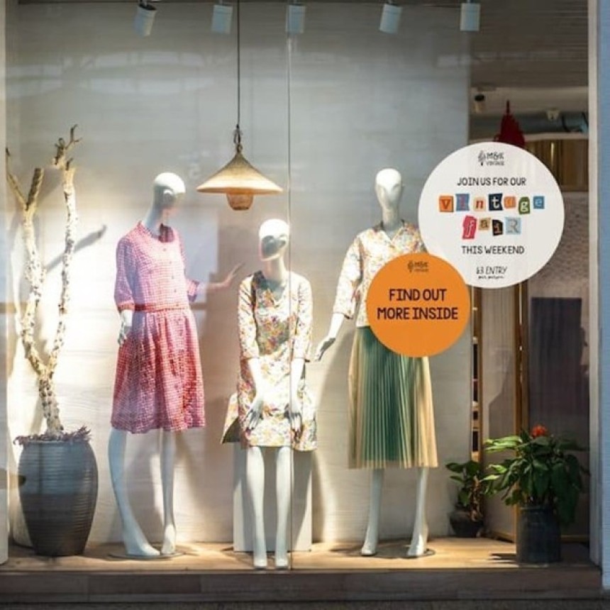 Witryna sklepu z trzema manekinami w sukienkach oraz plakaty promujące „Vintage Fair”; tekst: „JOIN US FOR OUR VINTAGE FAIR THIS WEEKEND… FIND OUT MORE INSIDE