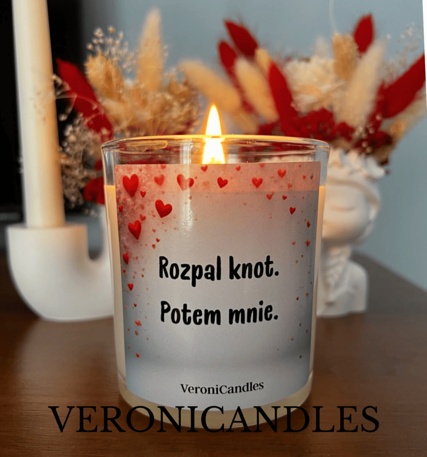 Zapalona świeca zapachowa VeroniCandles w szklanym naczyniu. Na etykiecie ozdobionej czerwonymi sercami widnieje napis: "Rozpal knot. Potem mnie."