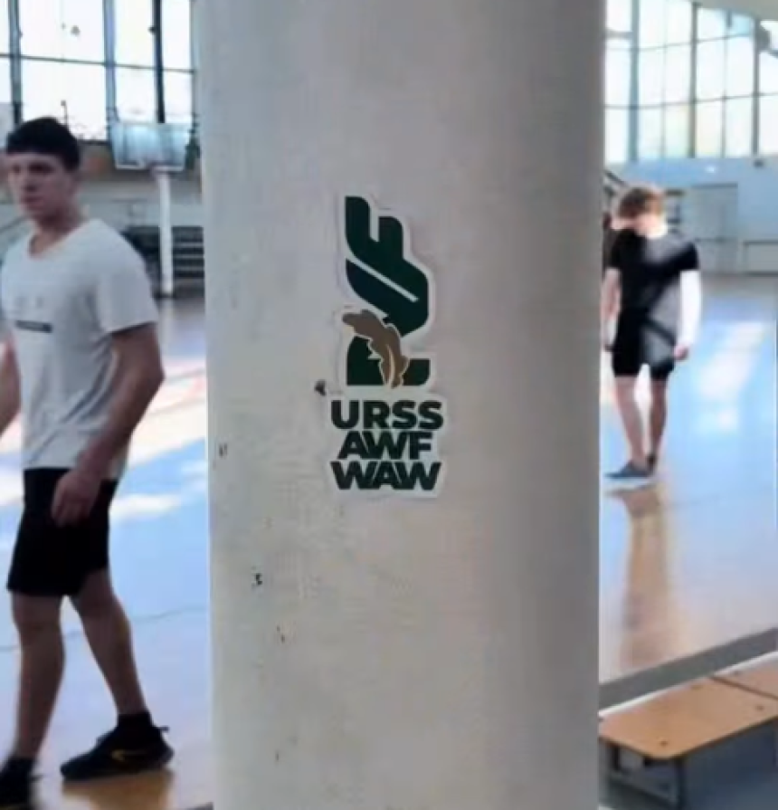 Naklejka z logo URSS AWF WAW na filarze wewnątrz sali gimnastycznej.
