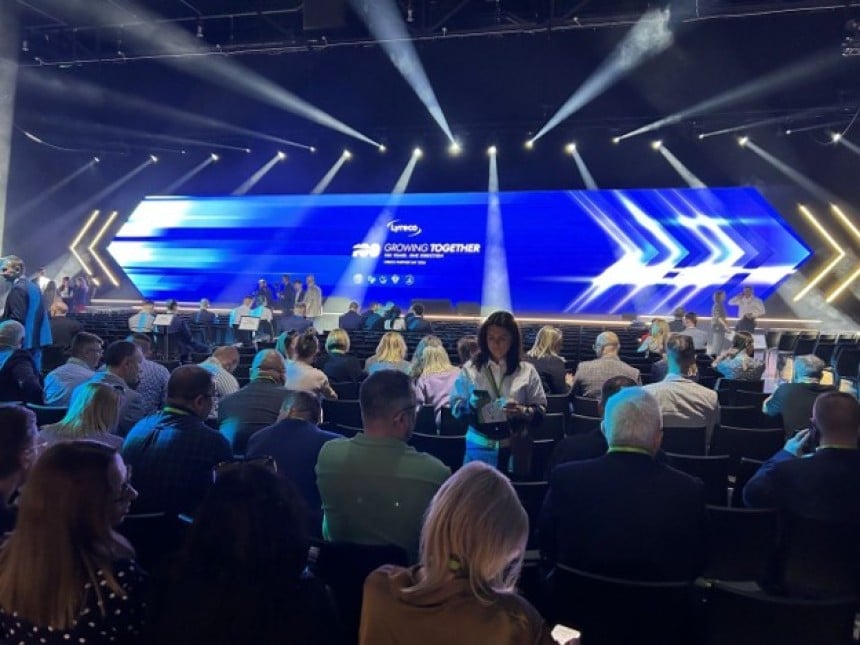 Szerokie ujęcie sali konferencyjnej wypełnionej publicznością. Uczestnicy siedzą zwróceni w stronę dużej sceny z panoramicznym ekranem LED, na którym widoczne jest logo Lyreco i hasło "Growing Together".