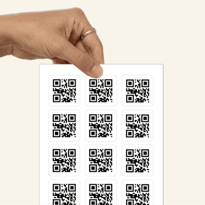  Dłoń trzymająca arkusz z dwunastoma naklejkami, na każdej z nich znajduje się ten sam kod QR.