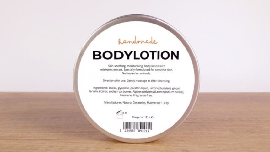 Okrągłe, metalowe opakowanie balsamu do ciała stojące na drewnianym blacie. Na białej etykiecie znajduje się tekst: "handmade BODYLOTION. Skin-soothing, moisturising body lotion with edelweiss extract. Specially formulated for sensitive skin. Not tested on animals. Directions for use: Gently massage in after cleansing. Ingredients: Water, glycerine, paraffin liquid, alcohol, butylene glycol, lanolin alcohol, sodium carbomer, Alpine edelweiss (Leontopodium nivale), limonene. Fragrance-free. Manufacturer: Nat