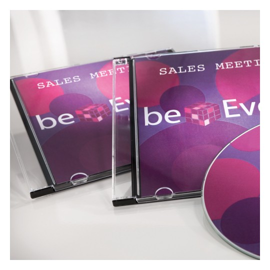 Obraz przedstawia dwa pudełka na płyty CD z tytułem „Sales Meeting” oraz płytę z kolorowym designem. Projekt zawiera okręgi w odcieniach różu i fioletu oraz tekst „beEven.”
