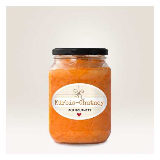 Obraz przedstawia słoik z Kürbis-Chutney z ozdobną etykietą. Chutney ma żywy pomarańczowy kolor, a słoik ma czarną pokrywkę. Na etykiecie na jasnym tle widnieje napis 'Kürbis-Chutney für Gourmets'.