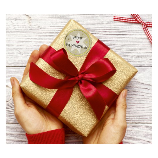 Obraz przedstawia prezent owinięty w złoty papier z czerwoną wstążką i kartką z napisem „Frohe Weihnachten”, co wskazuje na prezent bożonarodzeniowy.