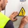Pracownik w stroju roboczym naklejający znak ostrzegawczy z ikoną błyskawicy na sprzęt elektryczny