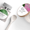 Flakon perfum z zielono-białą okrągłą etykietą, plastikowa łyżka oraz otwarte pudełko kremu z różowo, białą owalną etykietą na wieczku