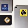 Naklejki kwadratowe oraz naklejka okrągła naklejone na różne sprzęty elektroniczne