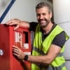 Mężczyzna w kamizelce odblaskowej stojący obok czerwonej metalowej szafki ze sprzętem przeciwpożarowym