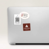Srebrny laptop z trzema naklejkami: białą z kodem QR i napisem ‘Delicious Coffee Shop’, owalną z grafiką kwiatów i napisem ‘Breeze Bloom’, oraz czerwonobrązową z ikoną płomienia i napisem ‘Steakhouse - Fine Grilled Dishes