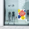 Witryna sklepowa z manekinami prezentującymi letnie ubrania. Na szybie widoczna naklejka z informacją o letniej wyprzedaży z napisem ‚SUMMER SALE’ oraz ‚BIS ZU 50% RABATT’ na kolorowym tle.