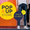 Osoba stojąca obok kolorowej tablicy reklamowej z napisami ‚POP-UP STORE’ oraz ‚SPACE TO RENT’ i zachętą ‚COME IN’ na żółtym i niebieskim tle. Widoczne są nogi osoby w dżinsach i białych butach.