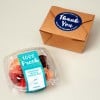 Brązowe pudełko zamknięte niebieską naklejką z napisem „Thank You” obok plastikowego pojemnika z plombą „100% Fresh” i świeżymi owocami.